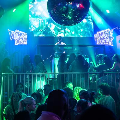 Dance floor with DJ booth, green lasers, spotlights and a large disco ball overhead.