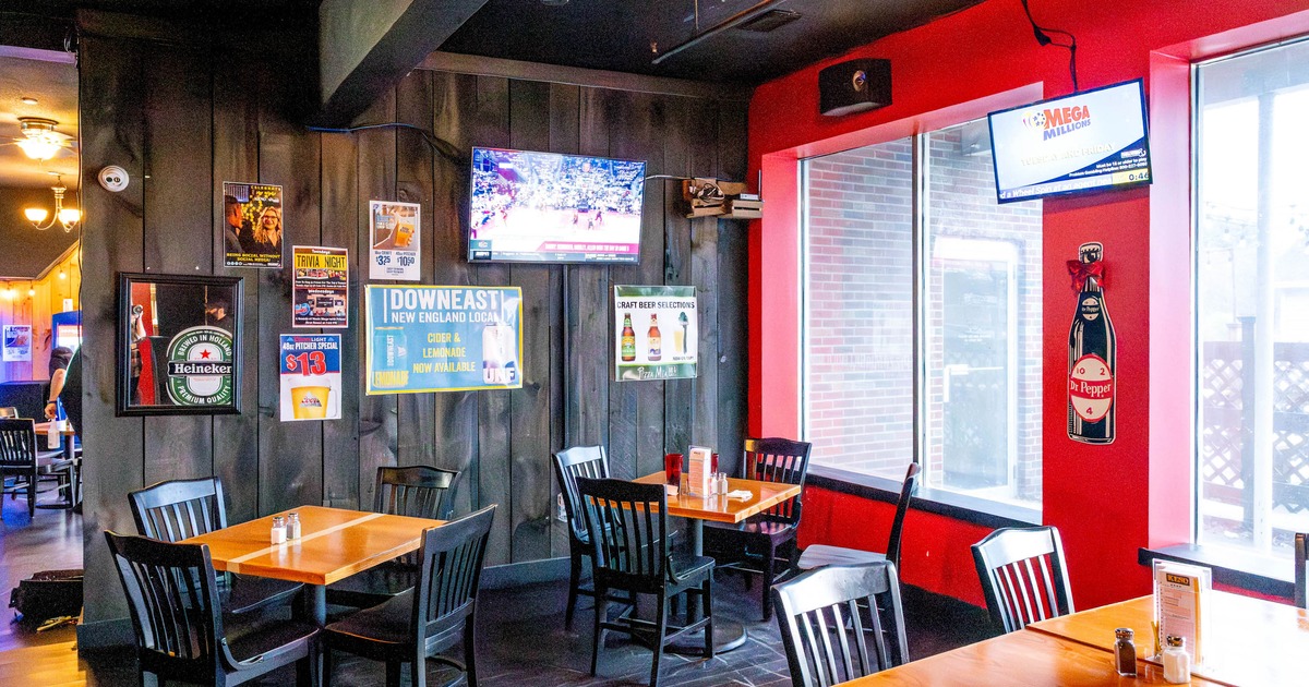 Interior of a casual restaurant with black walls, red accents, wooden tables, and mounted TVs