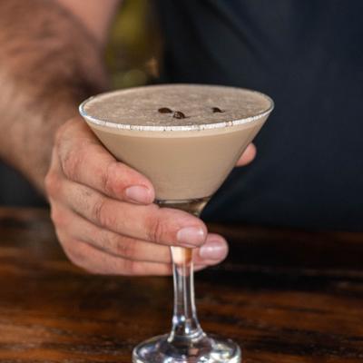 Hand placing a Espresso Martini cocktail on the bar counter.