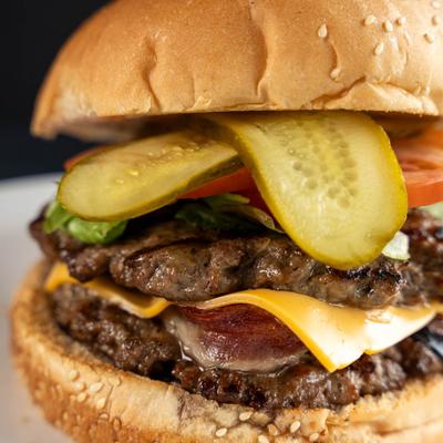 A close-up of a double cheeseburger with pickles, lettuce, and tomato.