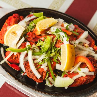 Chicken Tandoori with sliced onions, peppers, and fresh lemon wedges.