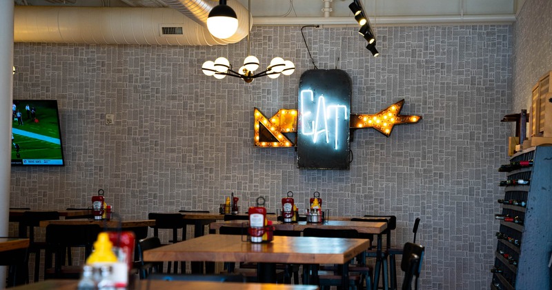 Interior, tables and seats, wine rack, TV and neon light sign on a gray mosaic wall
