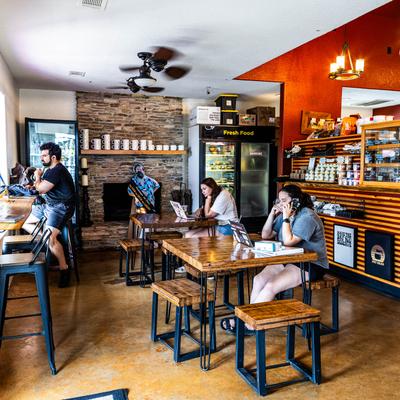 People sit at tables in a cafe with a stone fireplace and a refrigerated display case.
