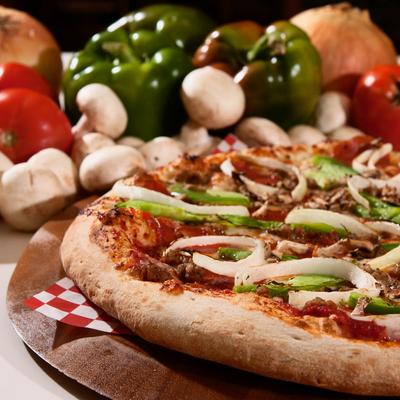 BBQ chicken pizza with honey BBQ sauce, onions, green peppers, against a vegetable background.