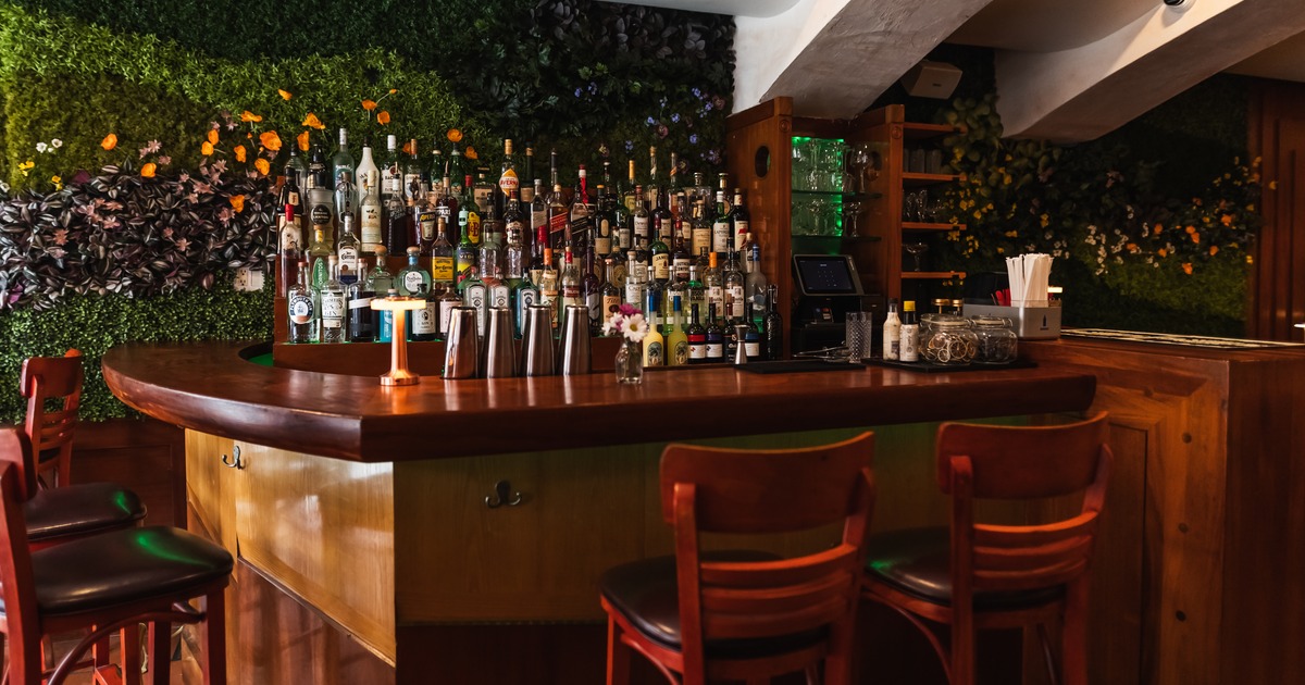 Bar area with a wooden counter, green flower wall, and liquor bottles