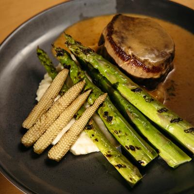 Beef tenderloin covered in a creamy sauce served with mashed potatoes, asparagus, and baby corn.