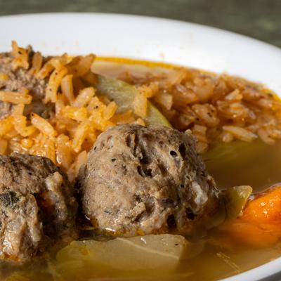 Close-up of meatball soup with rice, tomatoes, and carrots.