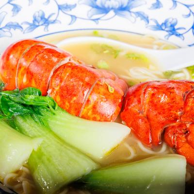 Close-up of lobster noodle soup with bok choy and lobster tail.