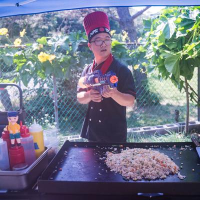 Chef holding a water gun behind an outdoor griddle with fried rice cooking.