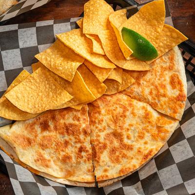 Top-down view of a sliced quesadilla with tortilla chips and a lime wedge.