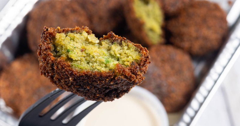 Close-up of a fork holding a crispy, brown falafel with a green, textured inside