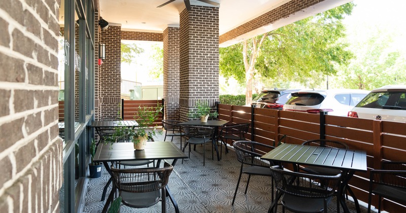 Outdoor cafe patio with brick walls, tables, chairs, and potted plants
