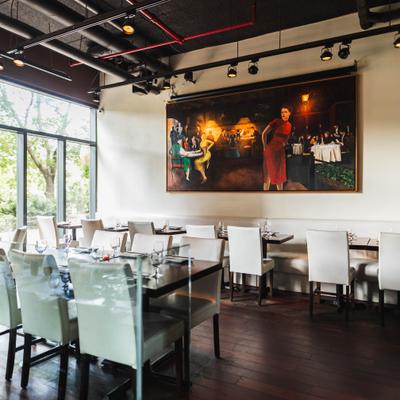 Dining area with white chairs, set wood tables, and a large colorful painting on the wall.