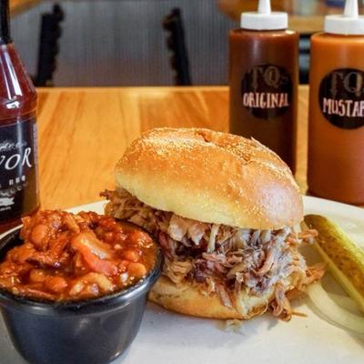 Pulled pork sandwich on a bun with baked beans and pickle on the side.