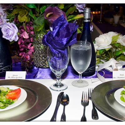 An elegant purple-themed formal dinner table setting with flowers, silverware, and glassware.