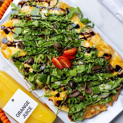 Flatbread pizza topped with arugula, tomatoes and balsamic glaze.