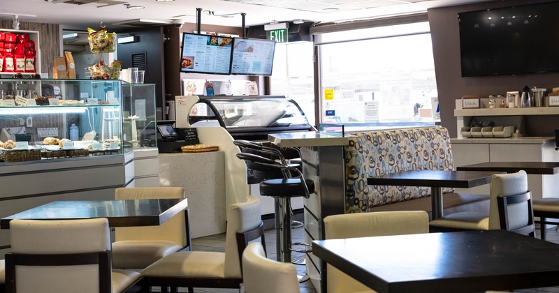 A modern interior with tables, a pastry display, digital menus and seating.
