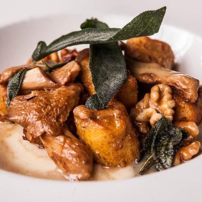 Braised potatoes with mushrooms and walnuts, garnished with sage leaves.