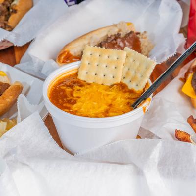 A bowl of chili topped with cheese and crackers, surrounded by hot dogs.