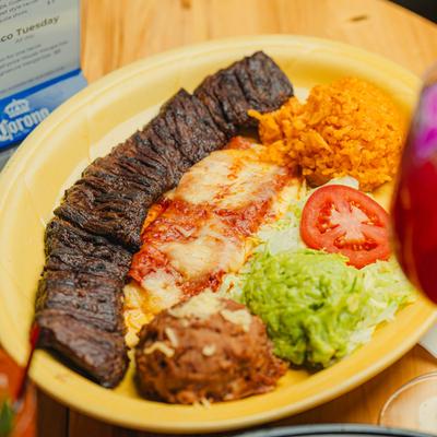 Mexican steak plater with rice, guacamole, beans. and enchilada.