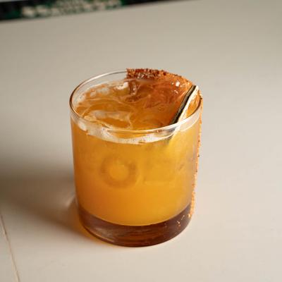 Chili-rimmed orange cocktail with a lime wedge garnish.
