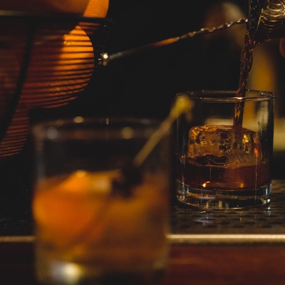Whiskey being poured into a rocks glass with one big ice cube.