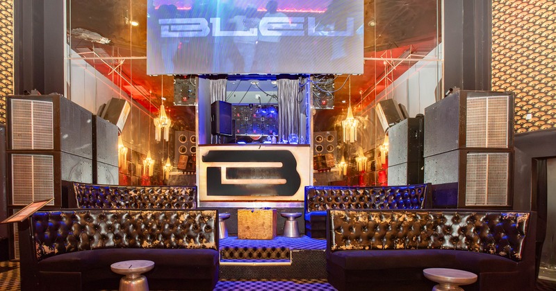 Interior featuring dark button-tufted leather sofas, a raised DJ booth and a sign