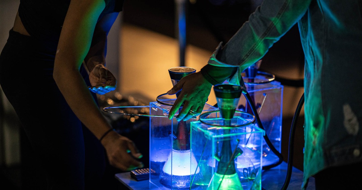 Two people standing by a table with glowing light hookahs