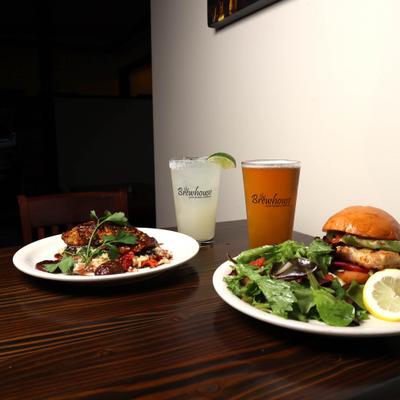 plate of Grilled salmon and plate of Grilled Chicken sandwich with house salad , Beer and margarita.