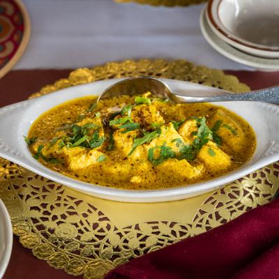 Chicken Korma dish served in an oval white dish atop a golden doily.