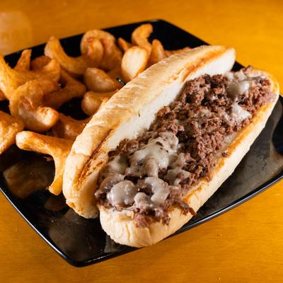 Philly Cheesesteak served on a black plate with Ava's sidewinder fries.