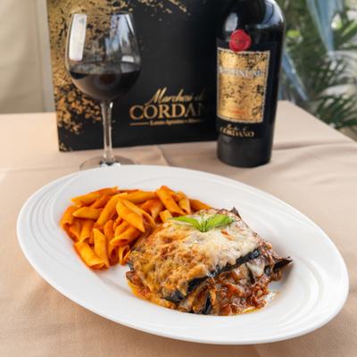 Eggplant parmigiana served with a side of penne pasta and red wine.