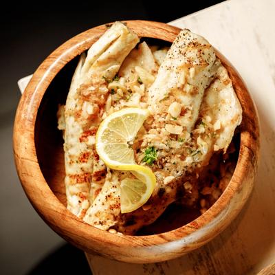 Grilled branzino fillets served in a wooden bowl with a lemon slice.