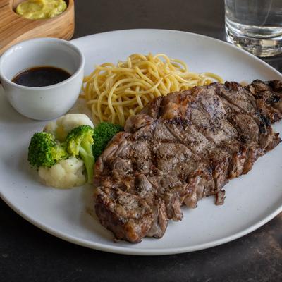 A grilled steak, pasta, broccoli and cauliflower, and a sauce on a white plate.