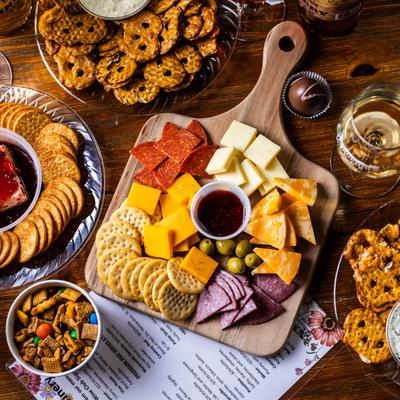 A snack spread featuring cheeses, meats, crackers, and a glass of wine.