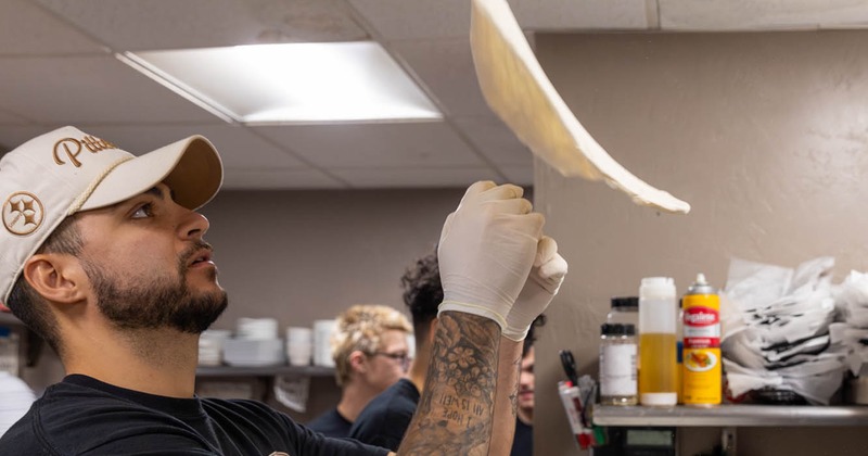 A pizza maker tosses pizza dough in the air
