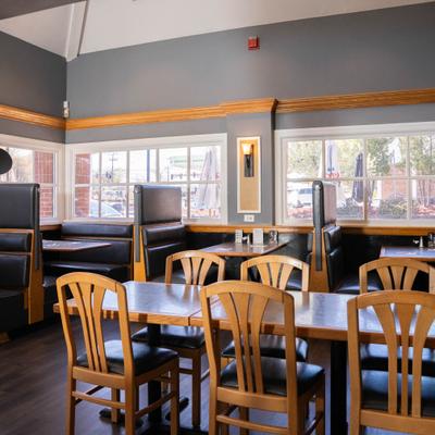 Interior featuring wooden tables, high-backed black booths and chairs with slotted backs.