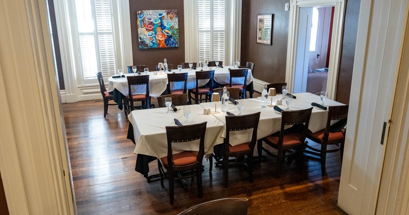 Dining room with two tables set for a meal, surrounded by wooden chairs