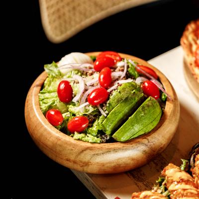A vibrant salad with avocado, tomatoes, and onions in a wooden bowl.