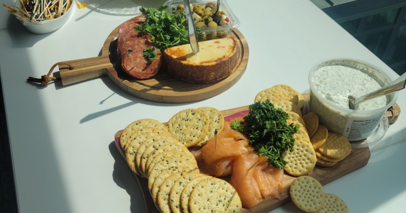 A platter including cured meat, a round of cheese, smoked salmon, crackers, and a dip or spread