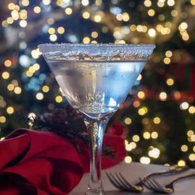 A martini cocktail glass on a table, Festive colorful bokeh lights are in the background.