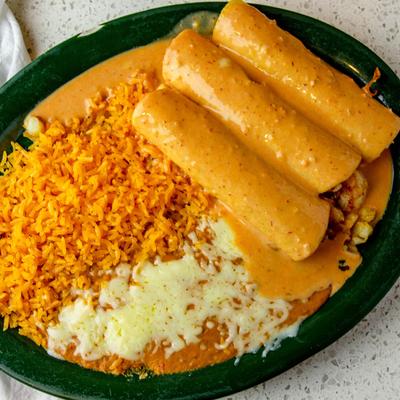 Shrimp bacon tacos, smothered in sauce, served with rice, and refried beans.