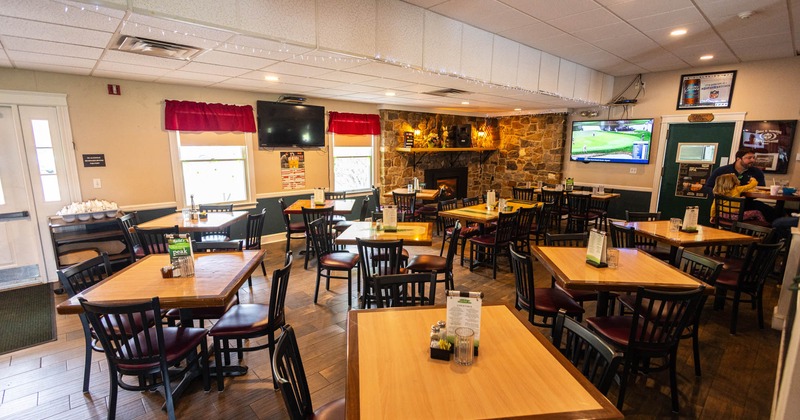 Casual, cozy restaurant interior with wooden tables and chairs, a stone fireplace, and two TVs