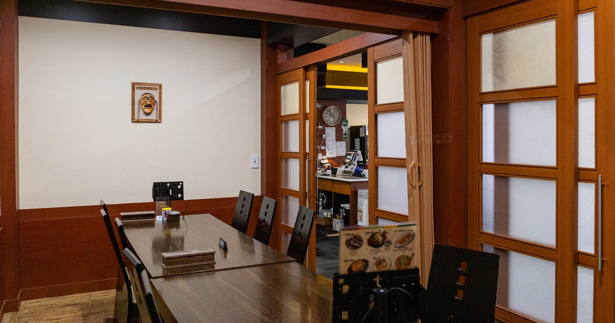 Wood-paneled dining room - a long table, black chairs, framed theatrical mask.
