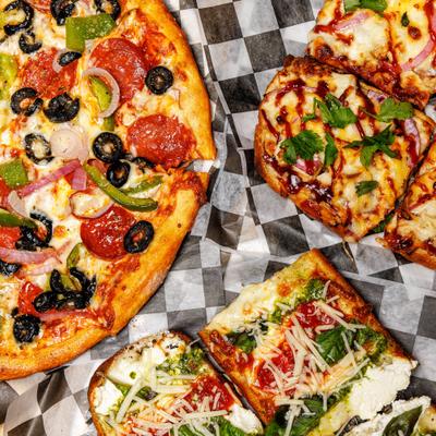 Variety of pizzas and flatbreads served on checkered paper, overhead view.