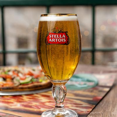 A glass of beer and a pizza in the background