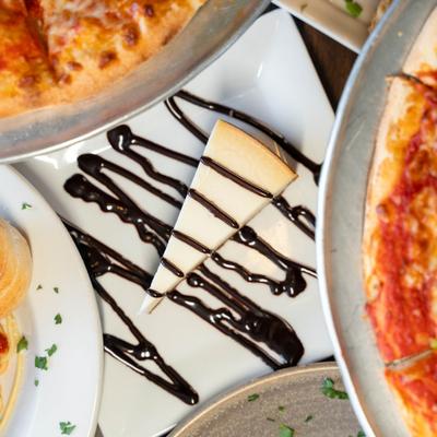 Chocolate cheesecake drizzled with chocolate, surrounded by assorted food dishes.