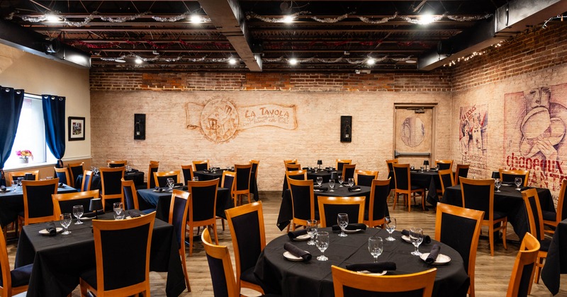 Restaurant dining room with exposed brick walls and neatly arranged tables with black tablecloths