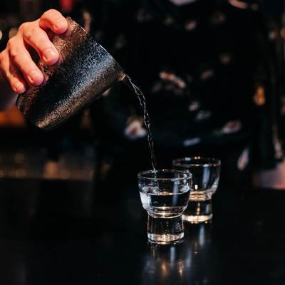 Bartender preparing a drink using a metallic shaker to pour into small glasses.