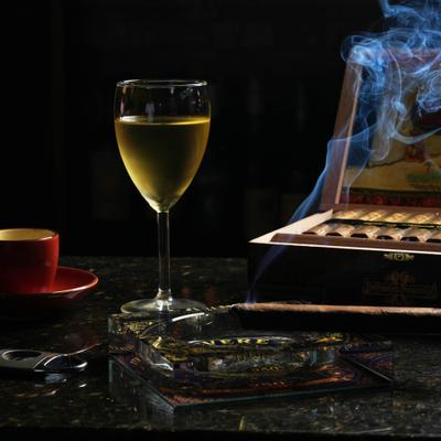 Lit cigar resting on an ashtray beside a glass of wine and an open cigar box.